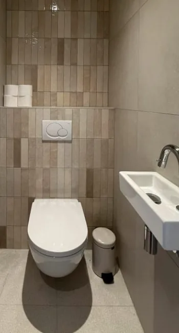 Witte fontein met chromen kraan naast een hangtoilet